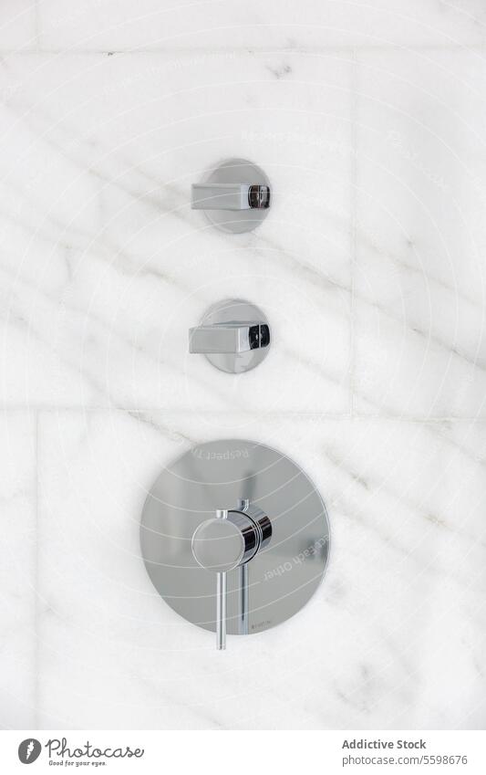 Silver levers installed on wall in bathroom penthouse stainless steel control marble luxury closeup silver metal mounted tile modern metallic knob handle