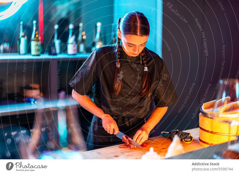 Confident skilled chef with long braids standing while cutting and preparing meat for dinner at sushi bar woman knife confident meal counter bistro chopping