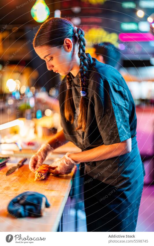 Side view of Confident skilled chef in black uniform and gloves standing at counter while making seafood at bistro woman cook sushi meal prepare illuminated