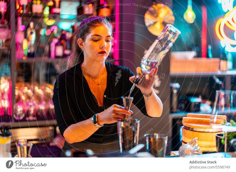 Focused Beautiful barmaid with blonde hair standing at bar counter while preparing cocktail at nightclub woman barkeeper alcohol jigger bottle confident pouring