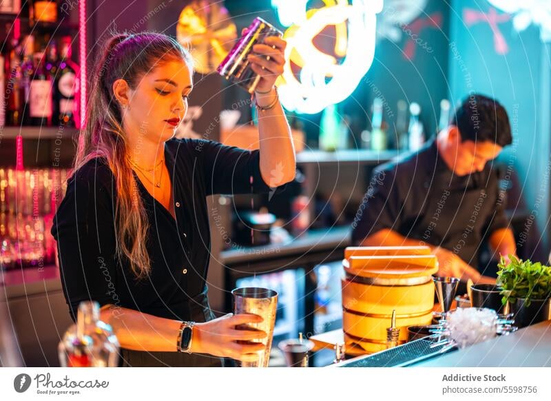 Side view of Confident barkeeper with blonde hair standing at counter while preparing beverage in cocktail shaker in bar woman barmaid mixing alcohol drink