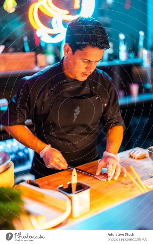 Focus Male chef in gloves and black apron standing while slicing meat with knife on counter at modern sushi bar man cook prepare seafood restaurant meal