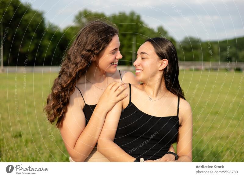 Two happy young women looking at each other in nature woman embrace smile field love companionship tender gaze affection summer outdoors connection relationship