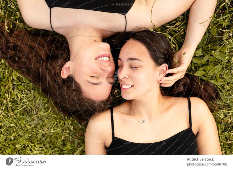 Happy women lying on the grass in a moment of affection with their eyes closed woman laughter LGBT pride lesbian couple connection love outdoors happiness