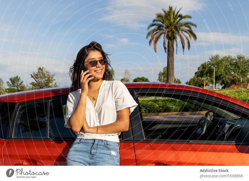 Happy woman leaning on car and talking over cellphone call smartphone happy attractive young orange sunny sunglasses mobile smiling sky beautiful communication