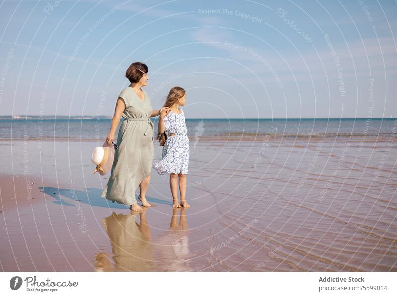 Beach stroll with mother and daughter beach sand sea reflection hat sky walk bond family moment woman child horizon water dress connection shoreline coast wave