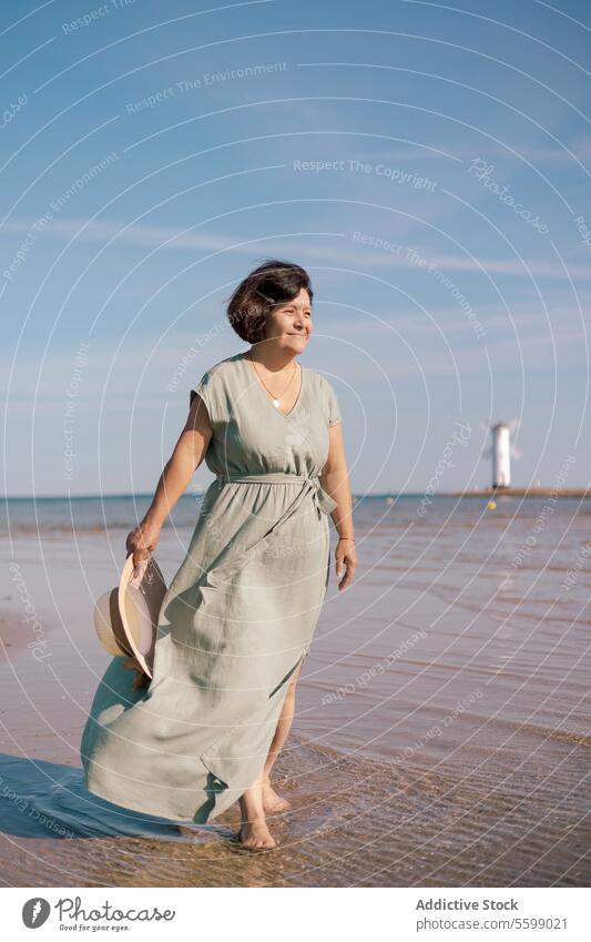 Woman gazing at sea horizon woman beach dress sun hat sand sky gaze summer coast water wave shield hand stand serene outdoors sunlight tranquility barefoot wet