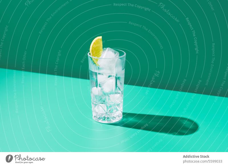 Refreshing glass of gin tonic with ice and lime on green water lemon shadow background minimalist clear refreshment beverage drink cold slice citrus healthy