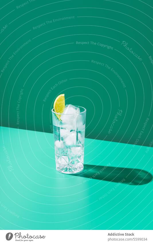 Refreshing lime gin tonic Glass on Teal Background glass lemon water ice teal background shadow refreshing beverage cool drink slice citrus hydration minimal