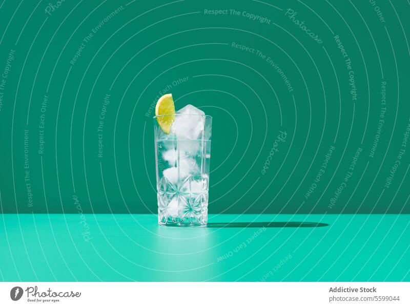 Refreshing gin tonic in a glass with ice on green background lime lemonade slice cold drink refreshment beverage water clear cube vibrant cool color minimal