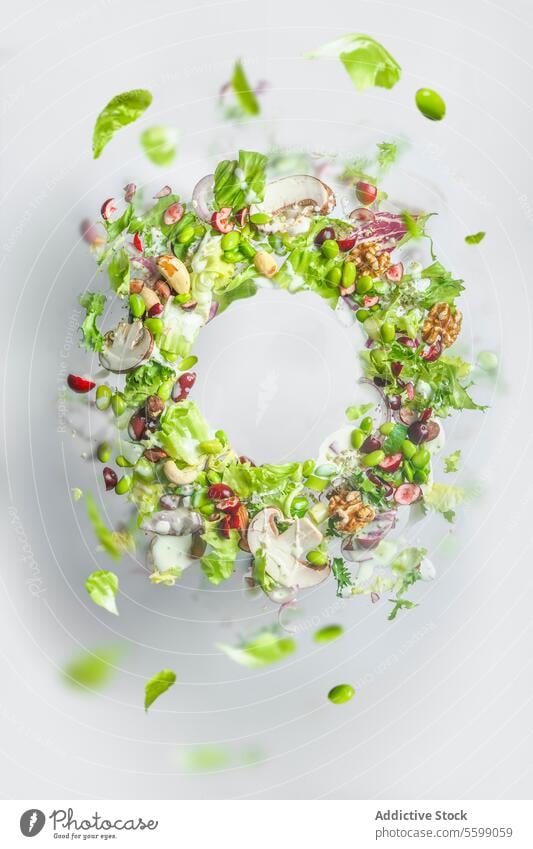 Circle frame of flying healthy green salad with lettuce, nuts, beans, dressing and vegetables. Balanced vegan food with copy space. Levitation of food circle