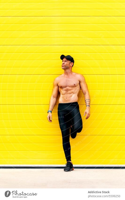 Shirtless man thinking while leaning on wall sportsman thoughtful cap shirtless looking away standing street yellow naked torso muscular strong pensive