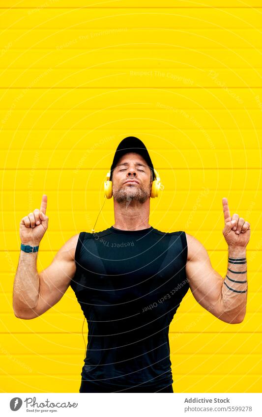 Calm athlete with headphones meditating over wall sportsman eyes closed listen music pointing up yellow calm portrait resting break exhausted strong gesture