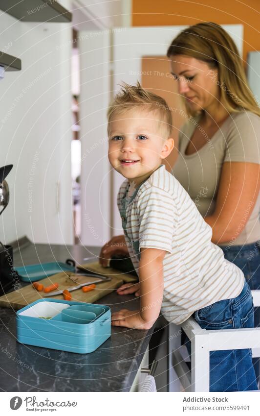 Focused happy mother and smiling child boy standing near kitchen platform at home kid son smile prepare lunch lunch box female young together love relationship