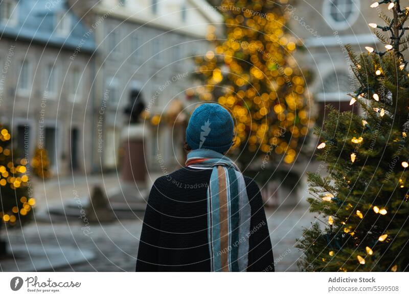 Contemplative figure admiring holiday lights in city in Quebec, Canada person winter hat christmas tree urban square back view atmosphere cozy twinkling