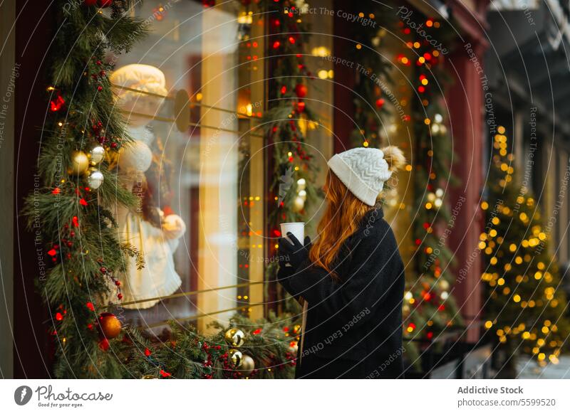 Woman admiring holiday window display in winter in Quebec, Canada woman coffee christmas mug decoration light festive knit hat coat shop storefront