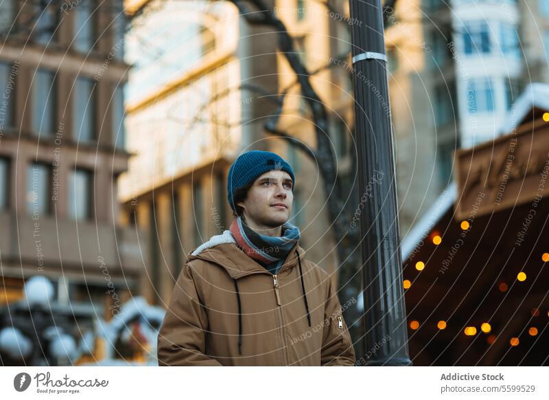 Young man contemplating in urban winter setting in Quebec, Canada young adult male casual outfit street city distance thoughtfully lamppost cold outdoor day