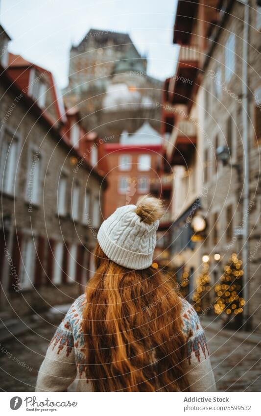 Woman in winter stroll through historic city alley quebec woman red hair beanie cobblestone street festive christmas market lights old travel tourism