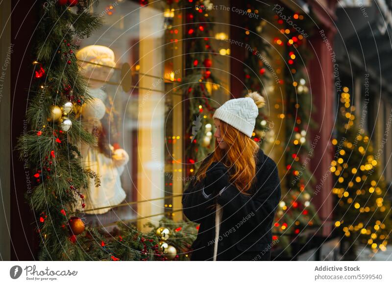 Woman admiring holiday window display in winter in Quebec, Canada woman christmas lights decorations cozy hat coat festive adorned city street shopping season