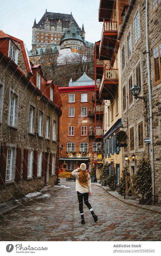 Charming old town street with a strolling tourist in Quebec, Canada woman walking cobblestone historic full body festive lights snow travel tourism winter