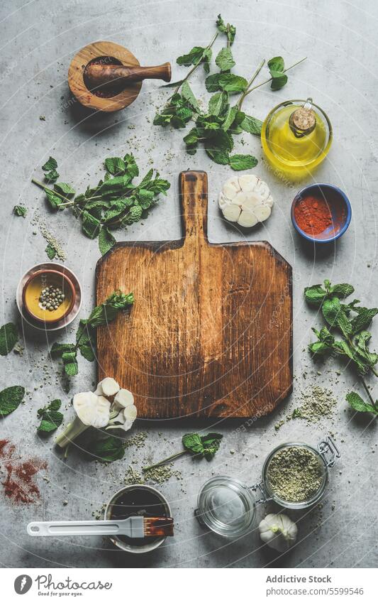 Empty wooden cutting board on grey concrete kitchen table with herbs ,spices, garlic,oil and mortar and pestle. empty preparing mint homemade marinade meat