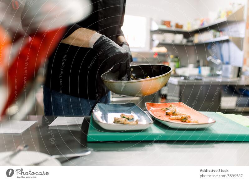 Side view of crop anonymous male cook in gloves standing at table and serving delicious broiled prawn with vegetables on plates in kitchen man chef food serve