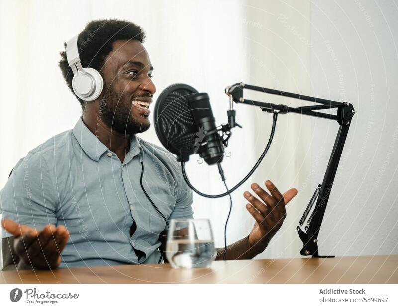 Black man recording podcast and gesticulating microphone speak talk gesticulate radio host male ethnic black african american broadcast audio headphones work