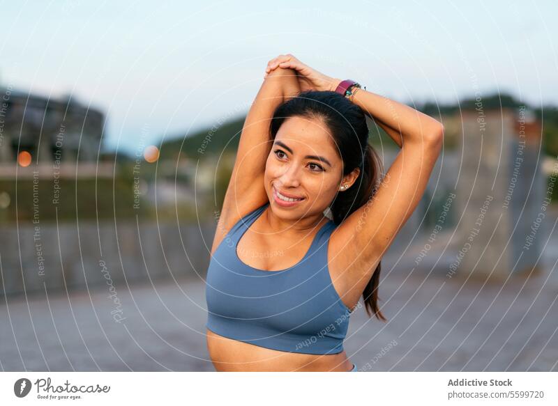 Smiling woman stretching outdoors after exercise latin american smiling workout fitness health wellbeing sportswear activewear athlete arms happy lifestyle