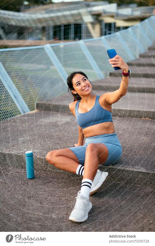 Latin American woman taking selfie during workout break latin american sportswear cheerful stadium stairs fitness exercise water bottle athletic leisure