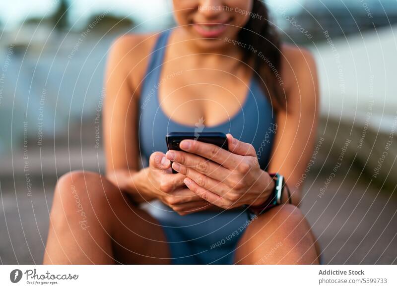 Smiling Latin American woman using smartphone outdoors after workout latin american technology sitting break exercise cheerful blurred background close-up