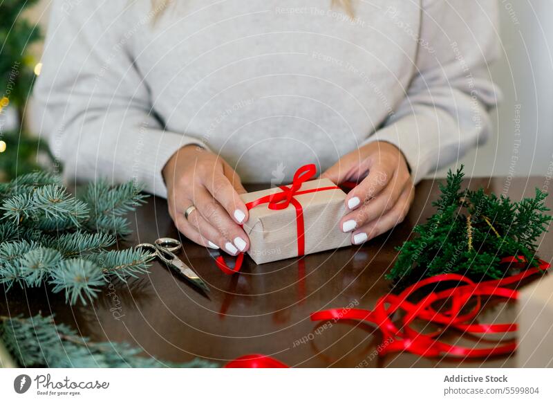 An unrecognizable woman is wrapping a Christmas gift in craft paper and a fir branch horizontal ribbon person decorating indoor happy female bow home surprise