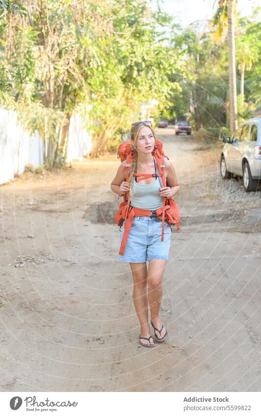Young traveling woman walking along dirty road with backpack activity adventure carefree casual confident cool daytime destination enjoy environment exotic