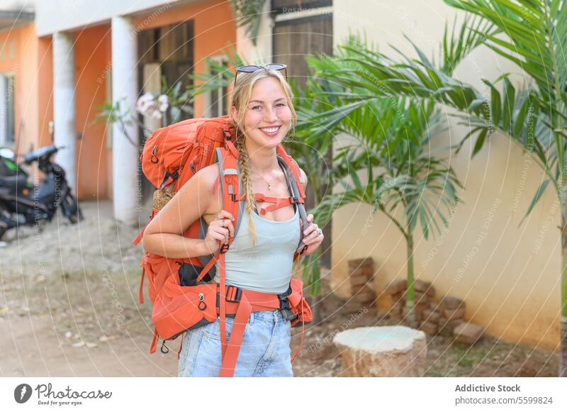 Happy young blonde woman standing with backpack on the road adventure backpacker beautiful blurred background casual cheerful copy space daytime delight