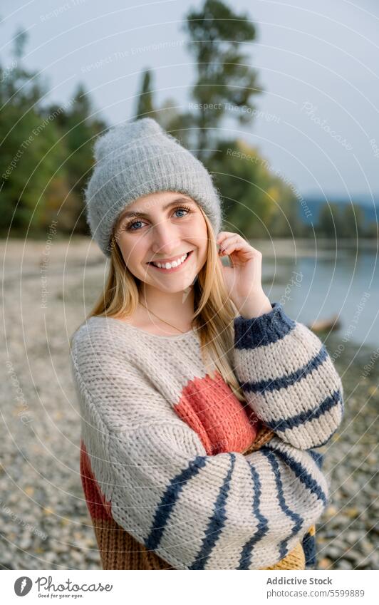 Smiling woman in warm clothes knitted female smile sweater happy cheerful lake nature countryside hat shore joy season style weekend positive rest relax young