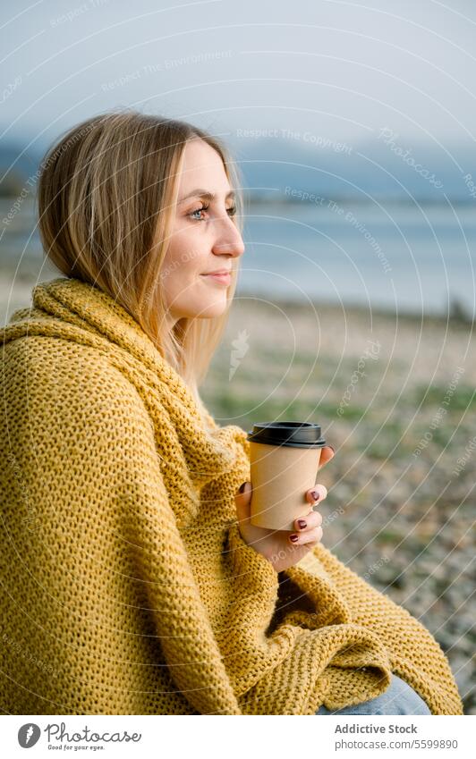 Young blond woman wrapped in blanket holding coffee mug at lakeshore person nature outdoors vacation sitting water adult lifestyle relaxation one person female