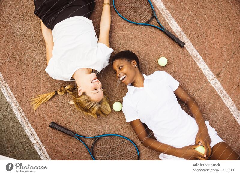 Portrait of two women laying on a tennis court. active lifestyle activity amateur athlete ball beautiful beautiful women cheerful competition diversity