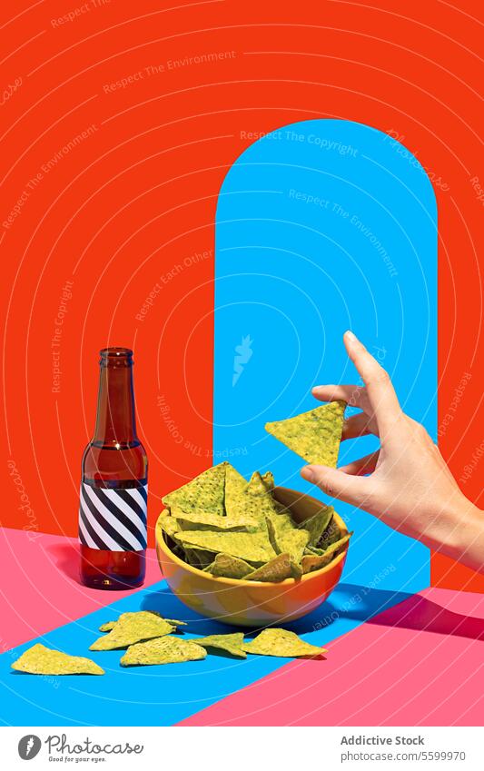 Unrecognizable hand picking nachos with colorful backdrop Hand chip bowl bottle red blue background snack food beverage reaching vibrant appetizer Mexican