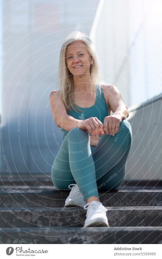 Active senior woman resting on steps after workout active fitness health wellness smiling sitting gray hair sportswear leggings tank top sneakers exercise