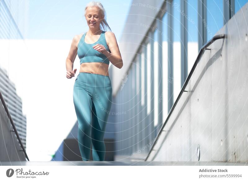 Senior woman jogging in urban environment senior mature health vitality active lifestyle exercise fitness sunny outdoors running athlete wellness sportswear
