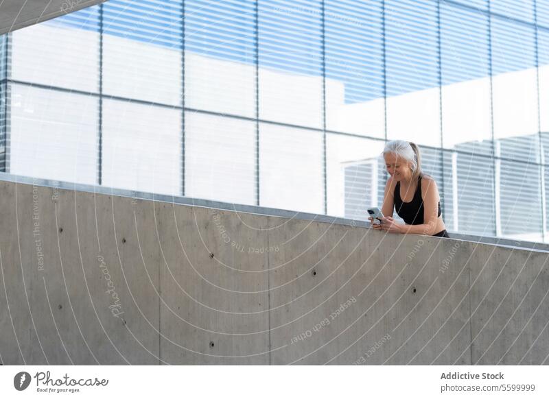Mature woman in sportswear using smartphone in modern city setting mature technology urban connectivity lifestyle contemporary building geometric pattern