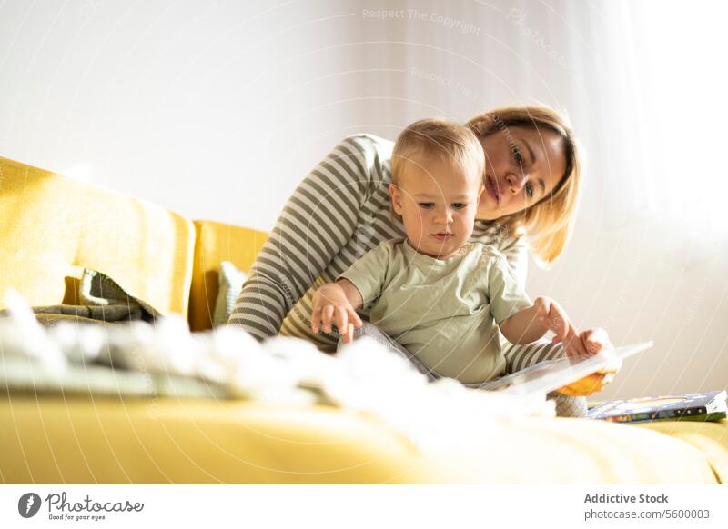Mother and toddler enjoying a book together on sofa mother reading home storybook child engagement caring comfortable couch family bonding learning education