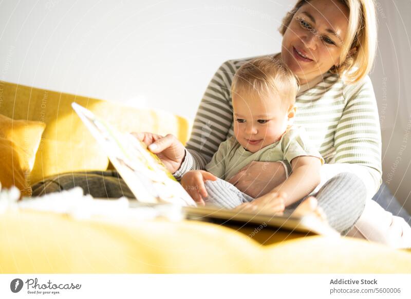 Mother and toddler enjoying storytime on a couch mother reading book picture book attentive cozy smiling seated yellow family bonding education child parent