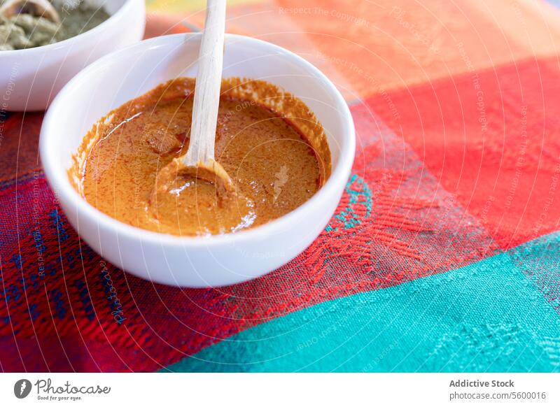 A bowl of yellow mole sauce with a wooden spoon on top of a colorful traditional tablecloth mexican food mexico oaxaca gastronomy authentic spicy chili pepper