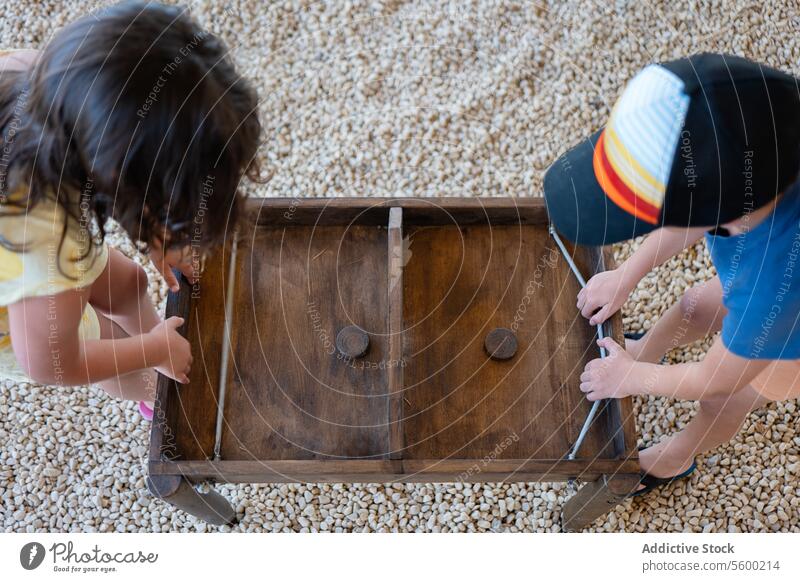 Two children working together on a wooden drawer teamwork fixing problem-solving collaboration overhead view young furniture repair indoor floor carpentry hands