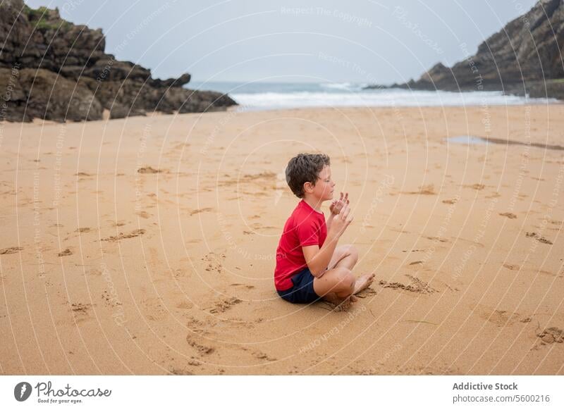 Young boy in contemplation on a foggy beach sand sea overcast cliff alone sitting coastal nature solitude outdoor reflective thoughtful young child shoreside