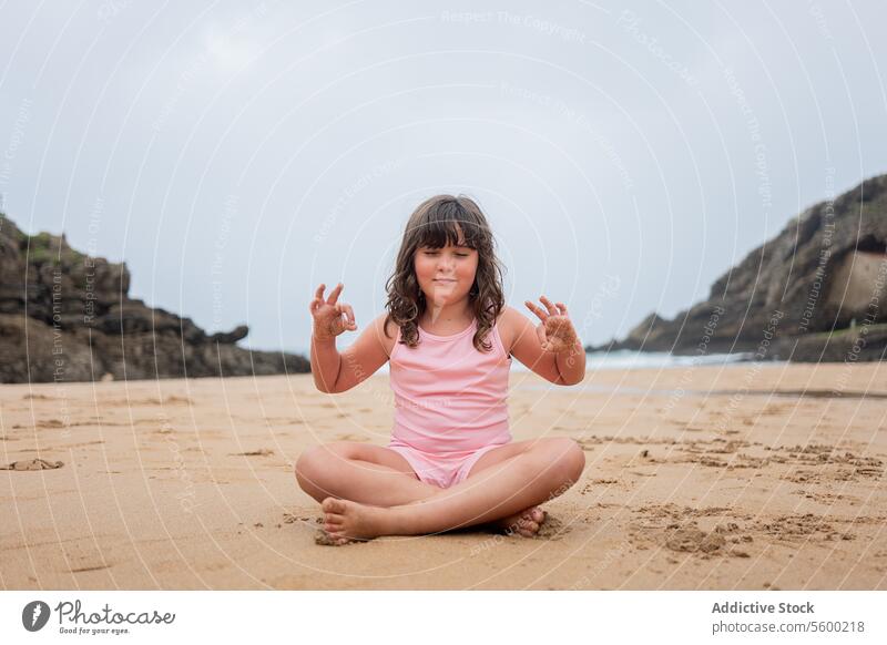 Young girl practicing yoga on a sandy beach children pose calm sea kid backdrop young cheerful cross-legged sitting wellness outdoor meditation health leisure