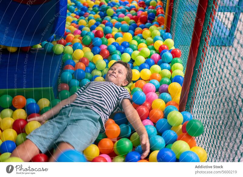 Young boy enjoying a colorful ball pit at an indoor playground child fun leisure activity kid playtime entertainment relaxation happy lying down multicolored