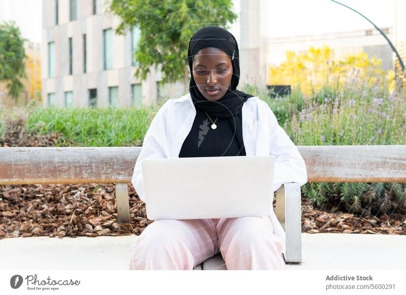 Female freelancer in hijab working on laptop in city businesswoman muslim serious concentrate tradition headscarf computer internet sitting bench new project