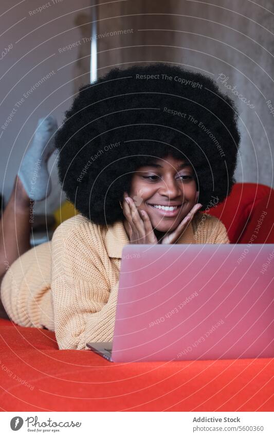 Smiling black woman typing on laptop using home sofa netbook comfort relax browsing female african american afro young cheerful smile couch rest lady weekend