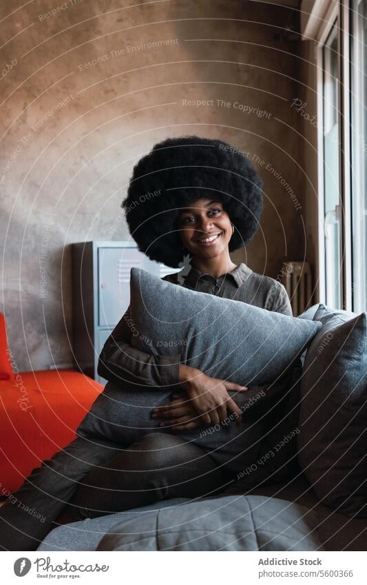 Dreamy happy black woman looking out window dreamy smile pensive cozy afro cushion feminine living room domestic cheerful appearance hairstyle charming brunette
